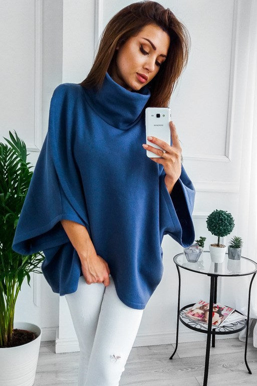 a woman in a blue ponchy sweater taking a selfie