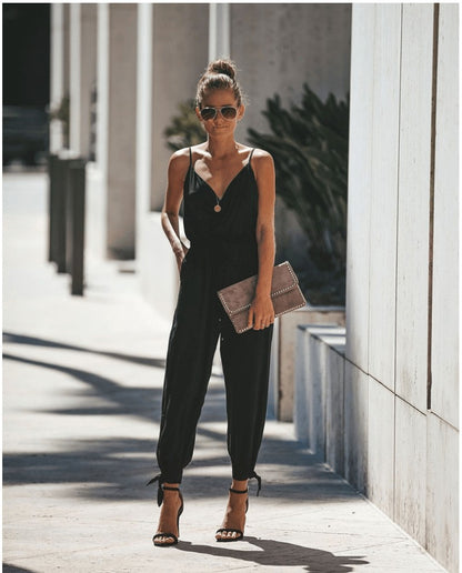 a woman in a black jumpsuit is standing on a sidewalk